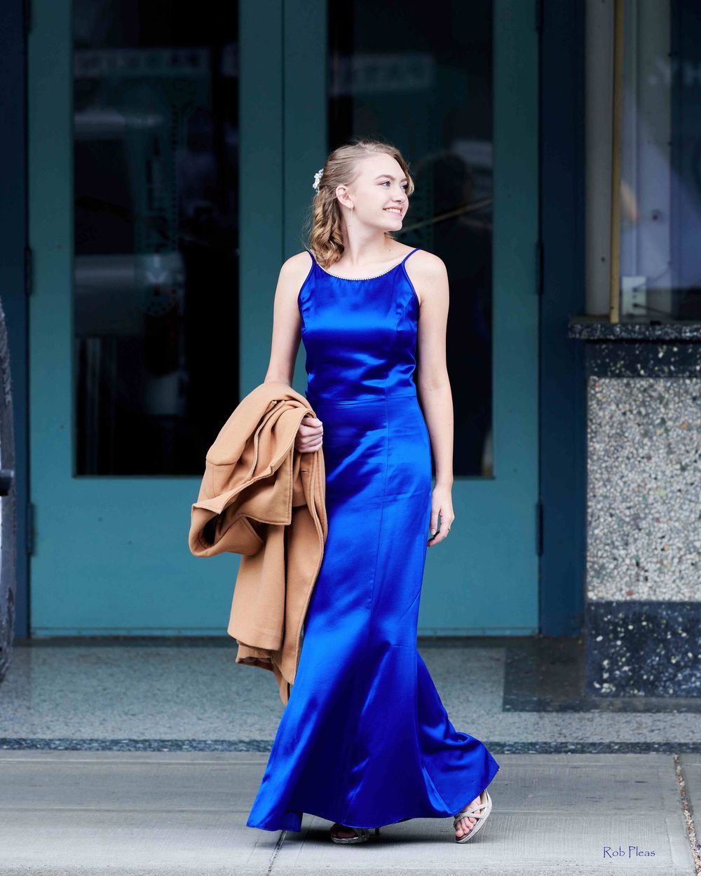High school senior female wearing blue dress while holding tan jacket in front of doors at Liberty Theatre in Puyallup, WA