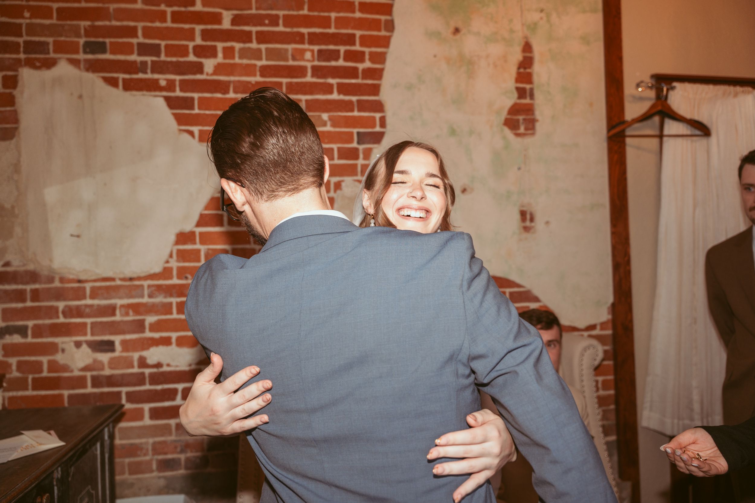 A couple shares a joyful embrace while dancing in a rustic brick-walled venue.