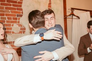 Two guests sharing an emotional embrace during a wedding celebration at a brick-walled venue.
