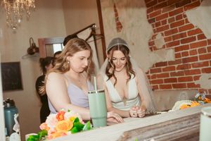 Two guests seated at a table with drinks and floral arrangements in a brick-walled reception space.