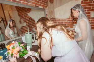 People in white dresses gather around a table with floral arrangements and mint green decor in a rustic brick setting.