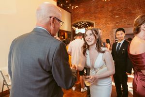 People gather at an indoor celebration with exposed brick walls and warm lighting as guests socialize with drinks.