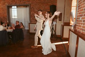 A couple performs an energetic dance move in a rustic venue with exposed brick walls and guests seated nearby.