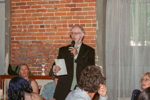 Speaker addresses wedding guests during reception in brick-walled venue.