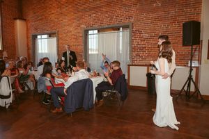 Wedding celebration in a rustic brick venue with guests seated at tables while speech is being delivered.