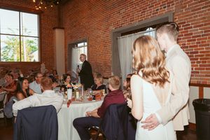 Wedding guests dancing in celebration at indoor rustic venue with exposed brick walls and natural lighting.