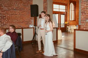 A couple poses together in front of a brick wall at their wedding reception venue.