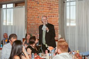 Someone giving an emotional wedding toast during reception dinner in industrial-style venue with exposed brick walls.