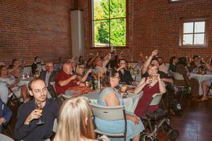 Engaged audience raises their hands while sitting at tables in a brick-walled event space.