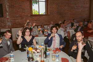 Reception guests raise their hands in celebration at tables during a wedding event.