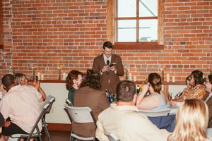 Someone delivers a speech to seated wedding guests in a brick-walled reception venue.