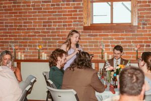 People gathered around tables having conversations during a social event in a brick-walled venue.