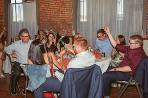 Party guests enjoy drinks and conversation around tables in a rustic brick-walled venue with string lights.