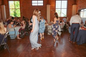 People dancing and celebrating at a wedding reception in a rustic brick venue with large windows.