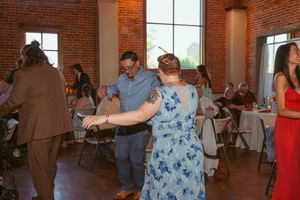 Wedding guests dancing and mingling in an industrial-style venue with exposed brick walls and large windows.
