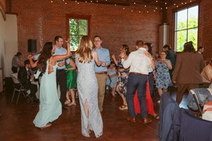 People dancing and socializing on a dance floor inside a rustic brick venue with string lights.