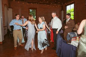 Wedding guests dance and celebrate in an exposed brick reception venue decorated with twinkling lights.