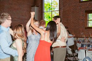 Party guests dancing and celebrating with raised arms in a rustic brick-walled event space.
