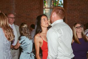 Wedding guests dance and socialize at a reception in a rustic brick-walled venue.