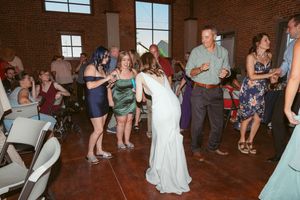 Wedding guests dance together at a lively reception party on a rustic wooden floor.