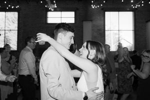 A couple shares a romantic dance at an indoor venue decorated with string lights while other guests dance in the background.
