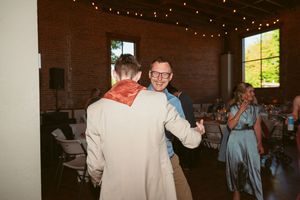 Two people share a dance at an indoor reception venue with string lights and exposed brick walls.