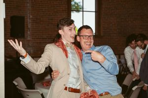 Two people laugh and gesture enthusiastically while enjoying a celebration in a brick-walled room.