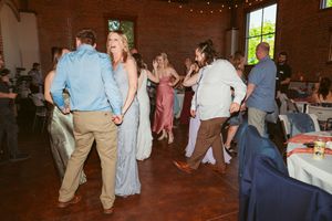 Wedding guests dancing together on a wooden floor in a brick-walled venue with twinkling lights overhead.