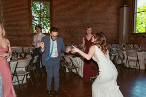 Wedding reception dance floor showing brick walls and white folding chairs in rustic indoor venue.