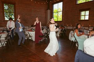Party guests dancing and celebrating at a rustic brick venue with string lights during a wedding reception.