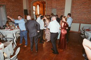 Wedding guests enjoying a dance party in a rustic brick-walled venue with string lights overhead.