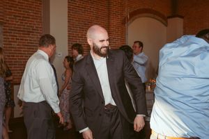 A group of people in business attire networking at a casual indoor gathering in a brick-walled venue.