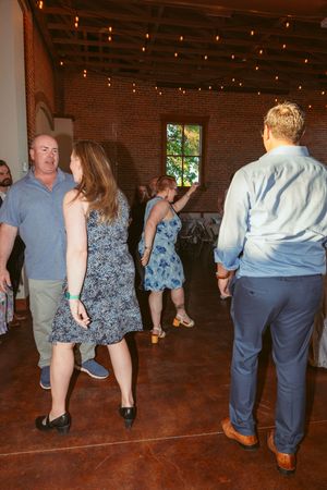 Wedding guests dance in a rustic brick venue decorated with string lights.