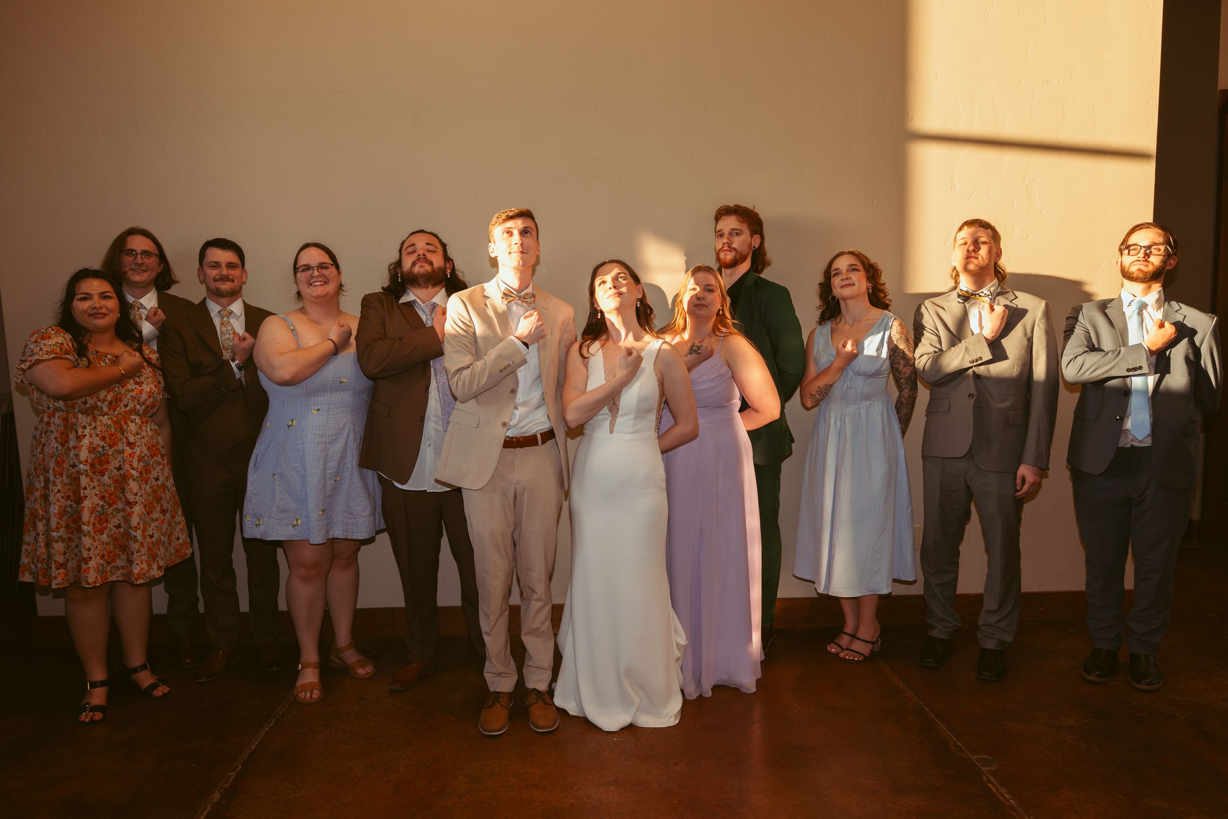 Wedding party lined up against a wall joyfully raising their glasses in celebration at a reception.
