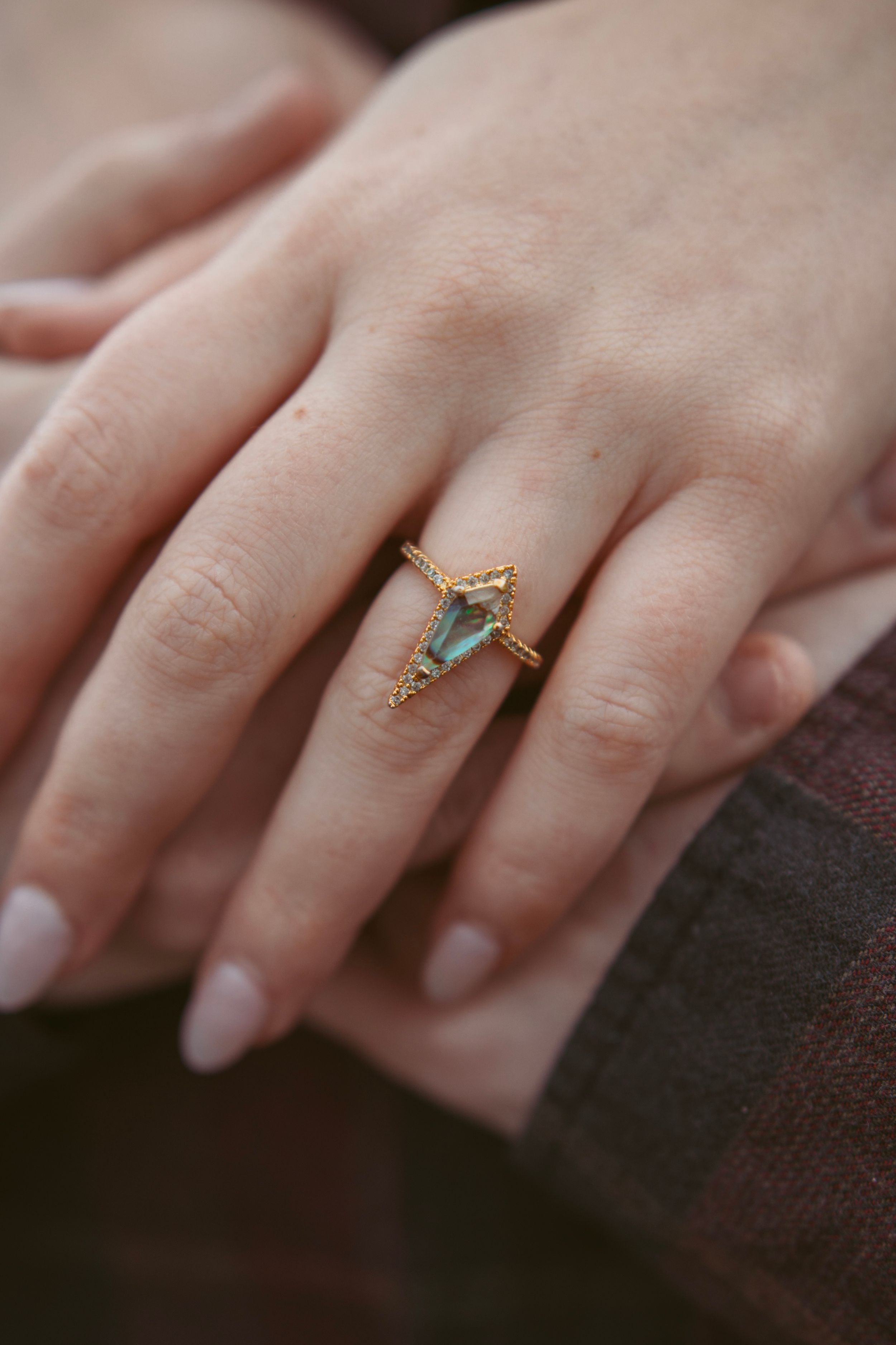 Close-up of a hand wearing a delicate aqua-colored ring against a dark fabric background.
