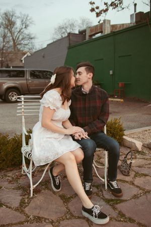A couple sits together on a rustic white metal bench sharing an intimate moment in a casual outdoor setting.