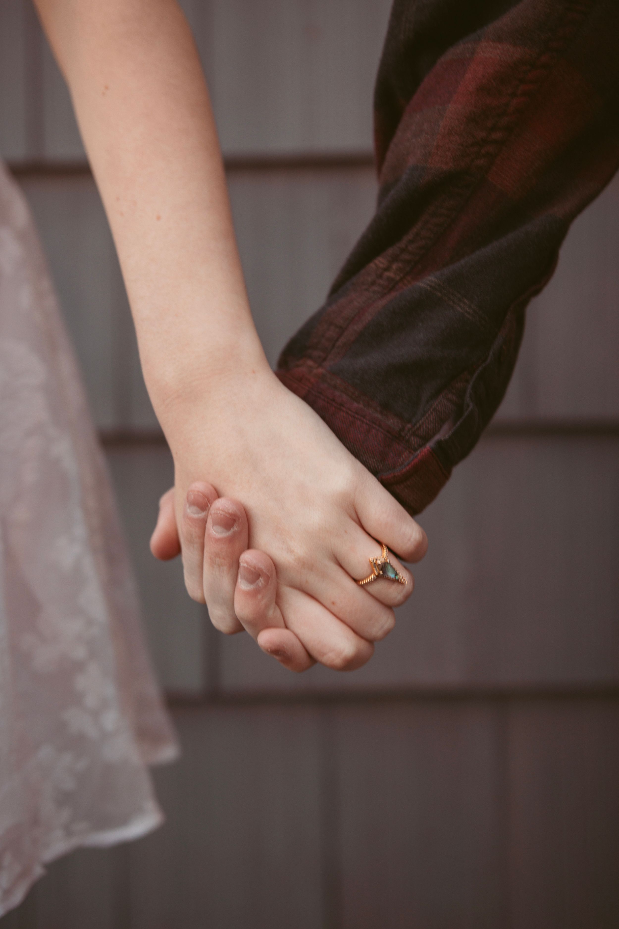 Close-up view of two hands clasped together with a ring, showing a romantic moment against a grey background.