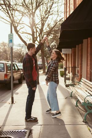 Two people share intimate moments while walking along a storefront sidewalk with black awnings overhead.