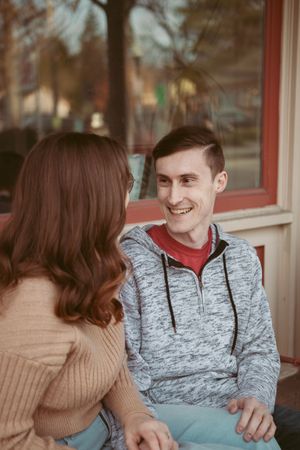 Two people in casual winter wear share a warm conversation while sitting outdoors.