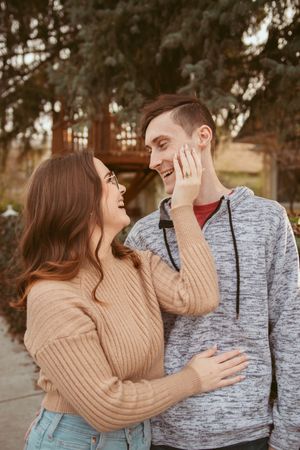 Couple in casual sweaters embracing and laughing together during outdoor photoshoot.