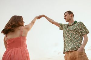 A couple in summer attire dance together against a bright white background.