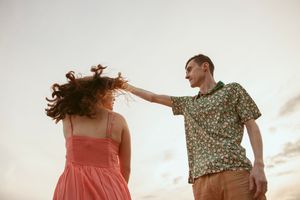 Couple in floral and coral outfits dancing together against bright sky.