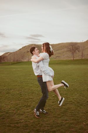 Couple spinning and embracing joyfully in a green field with mountains in the background.