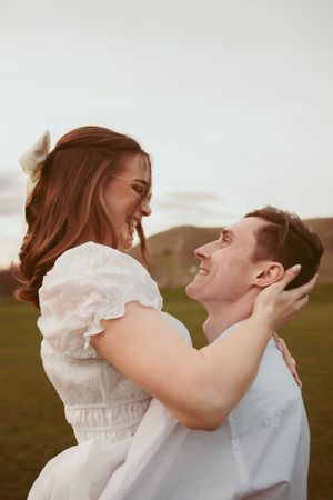 A romantic couple sharing playful moments outdoors in a sun-lit field with vintage-inspired outfits.