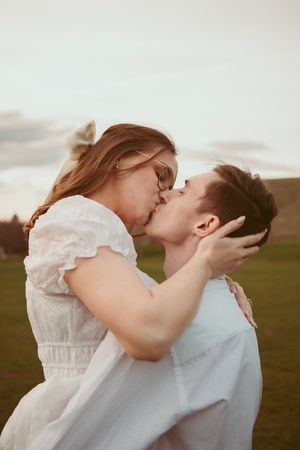 Couple in white and light clothing sharing intimate kiss in golden outdoor setting.