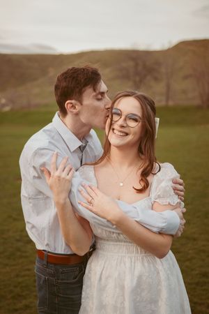 A couple shares a joyful moment in a green field with rolling hills in the background at sunset.