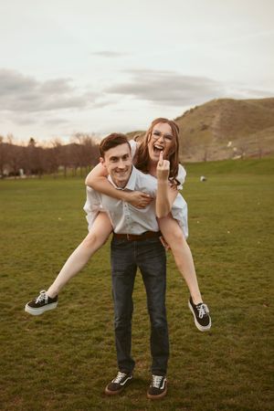 Two young people sharing a playful piggyback ride moment together in a grassy field during sunset.