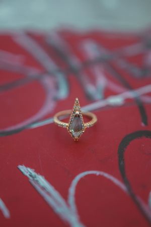 Delicate vintage-style ring with grey moonstone and small diamonds on ornate gold band against red patterned background.