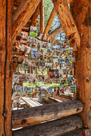 Rustic wooden shelter with photographs hanging from strings between tree trunks creating a memory wall display.