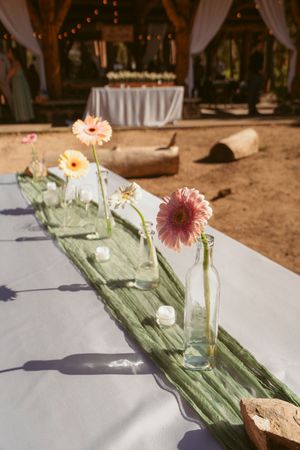 Elegant table settings featuring pink gerbera daisies in glass vases arranged on sage green table runners.